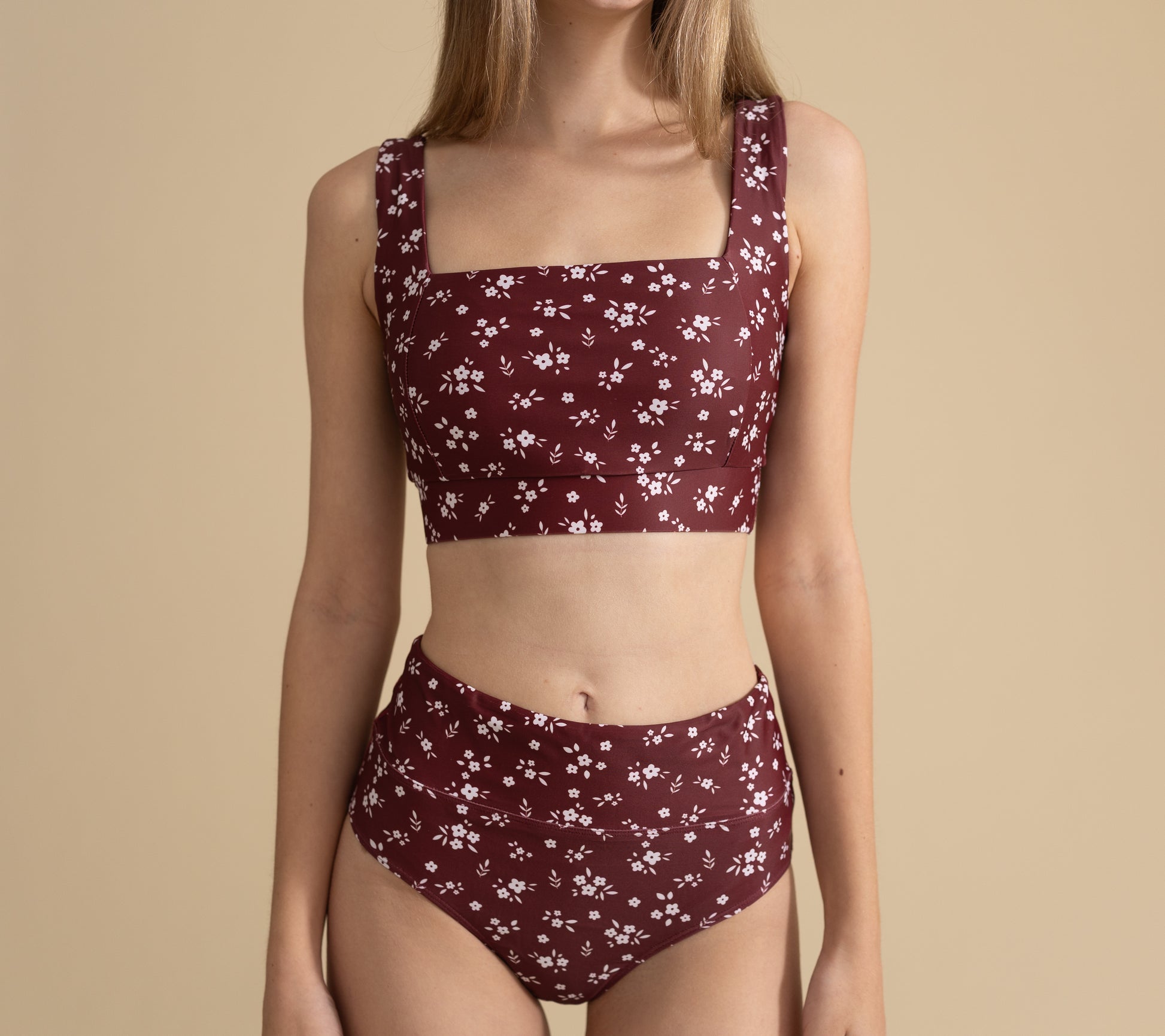 Woman wearing a maroon floral bikini set on a beige background