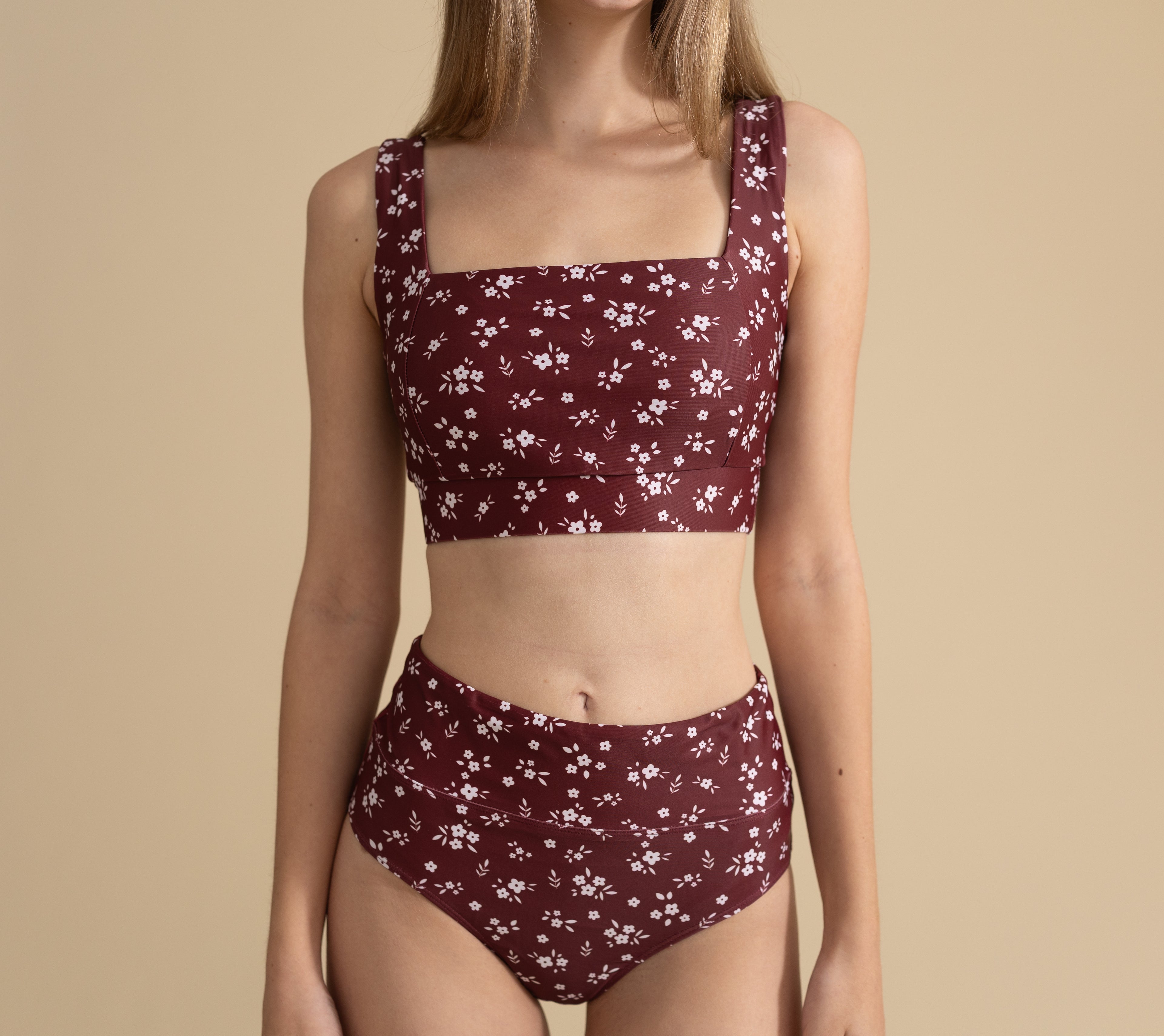 Woman wearing a maroon floral bikini set on a beige background